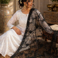 Woman in a white outfit with a black lace dupatta sitting indoors.
