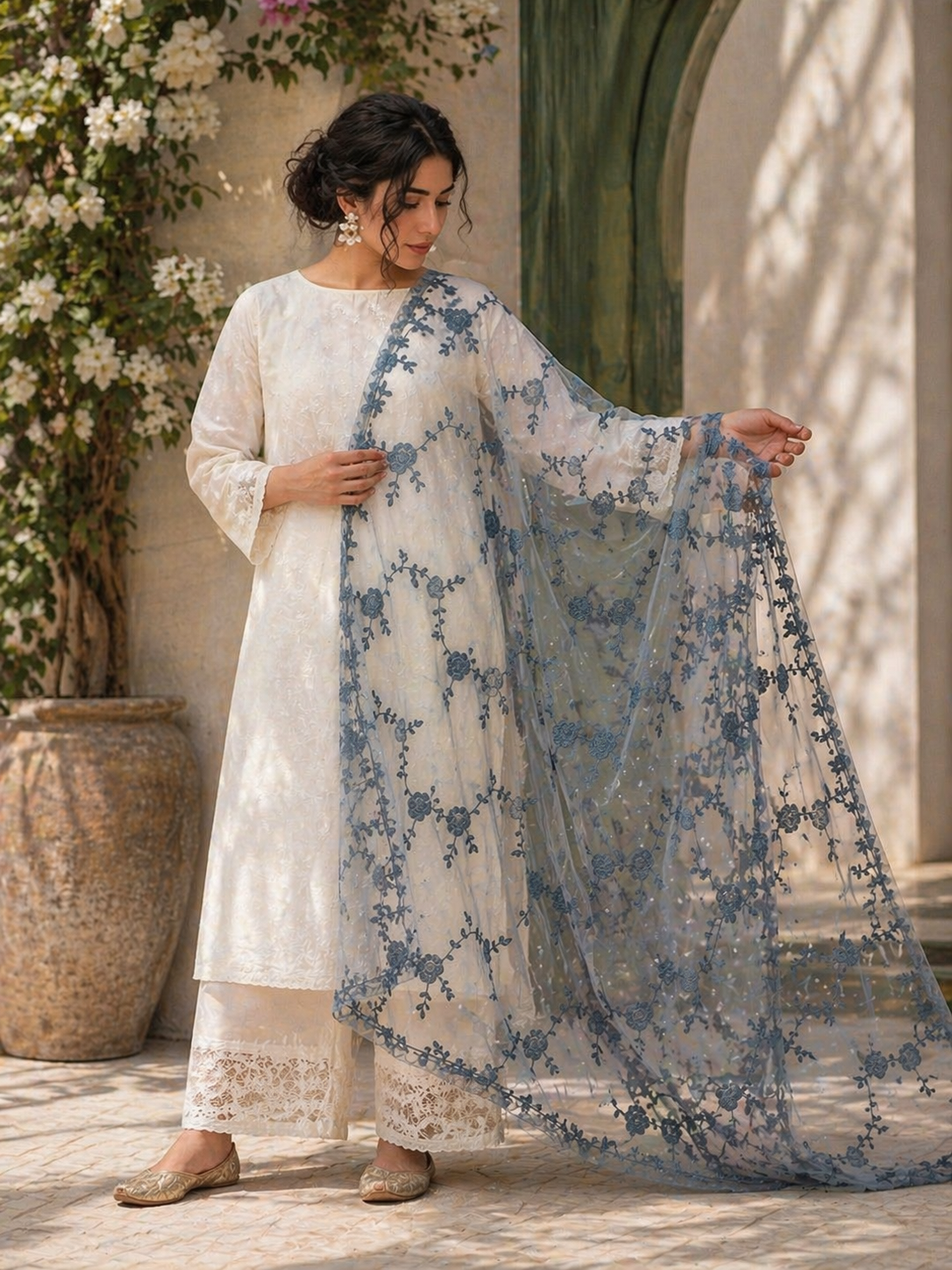 Woman in a white traditional outfit with a blue floral dupatta standing outdoors.