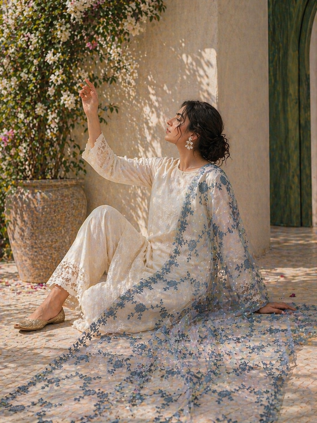 Woman in a floral dress sitting on a rug outdoors with flowers and a building in the background