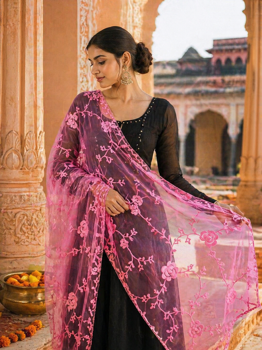 Woman wearing a black dress with a pink embroidered dupatta in front of an architectural background