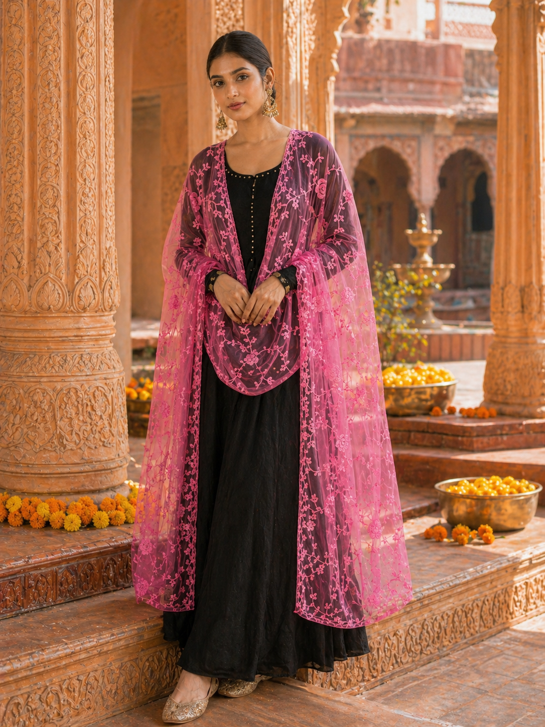 Woman in a black dress with a pink dupatta standing in an ornate architectural setting.