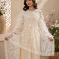 Woman wearing a beige embroidered outfit with a sheer dupatta in a decorative setting.
