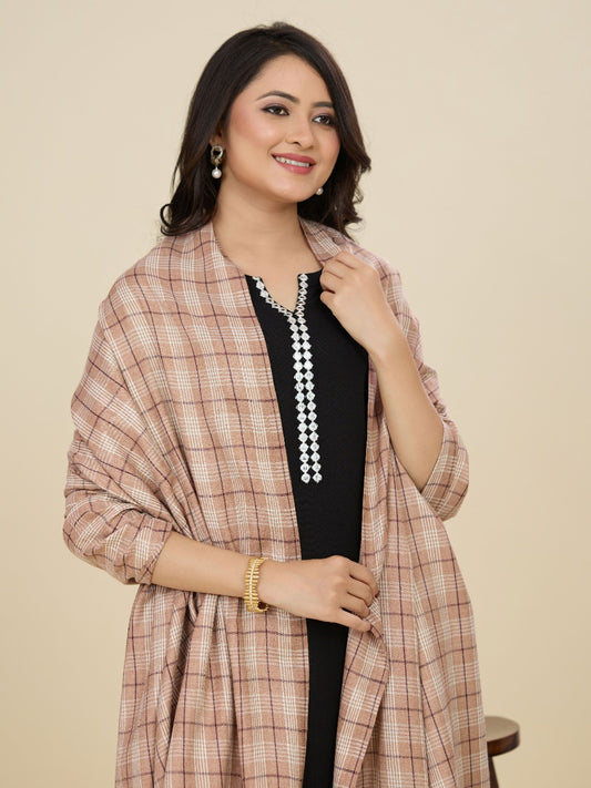 Woman wearing a checkered shawl over a black outfit with a beige background