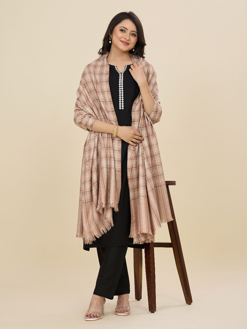 Woman wearing a plaid shawl over a black outfit on a beige background