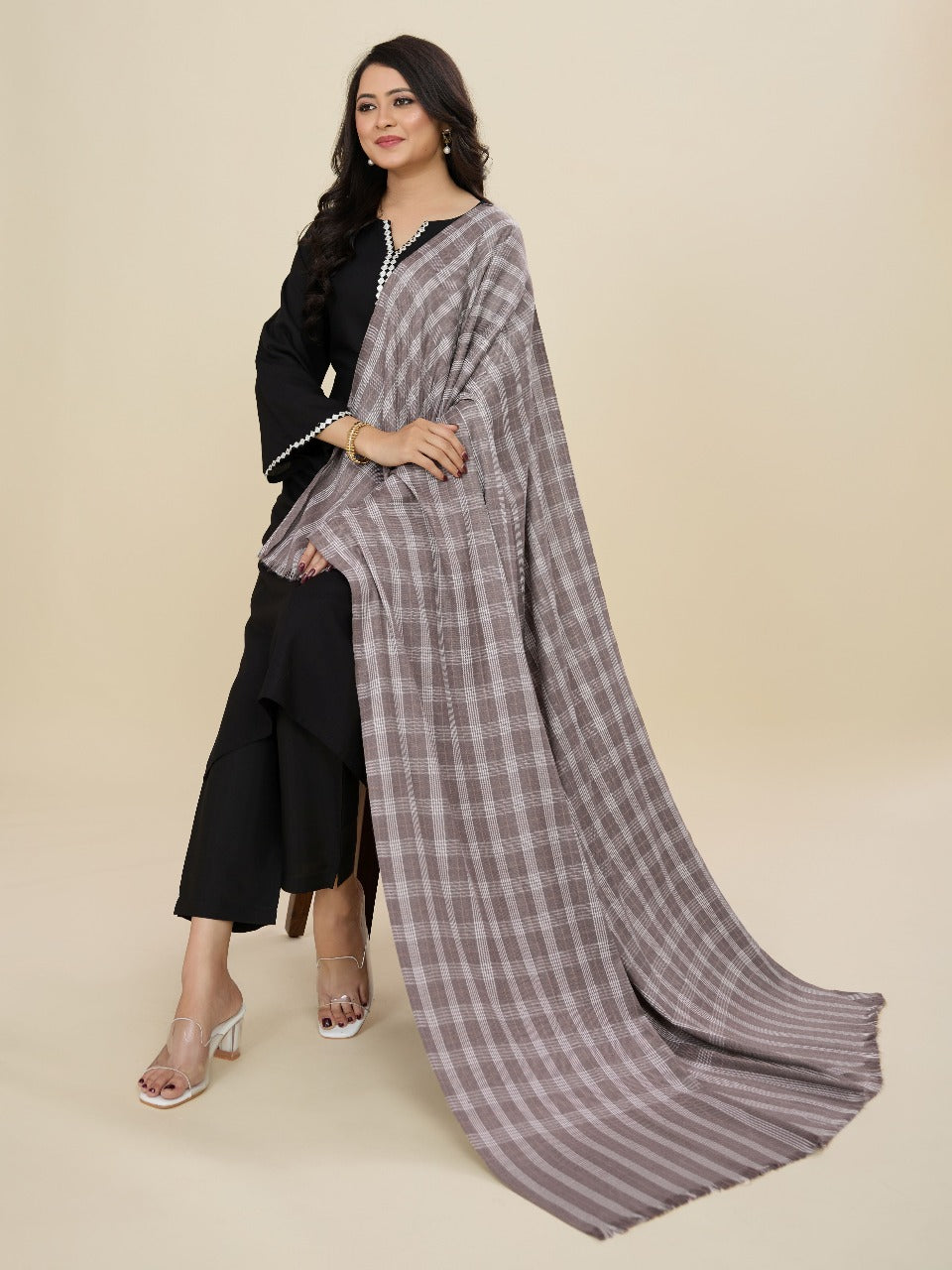 Woman wearing a black outfit with a gray checkered dupatta on a beige background
