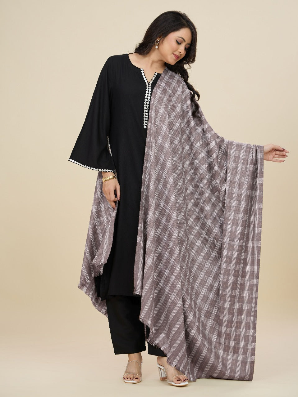 Woman holding a checkered scarf with a black outfit on a beige background