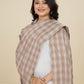 Woman wearing a brown checkered shawl over a white outfit against a beige background