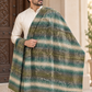 A man wearing a cream kurta and draped over his shoulder is a large woven shawl with horizontal stripes in green, teal, olive, and cream, featuring a fringed edge.
