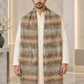 A man wearing a long, patterned scarf draped over his shoulders over a cream-colored kurta, standing in a modern indoor setting with marble walls and columns.