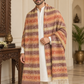 A man wearing a white kurta and trousers draped in a long, multicolored striped shawl with fringe, standing in an ornate indoor setting.