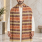 A man wearing a long striped woolen shawl with cream, orange, brown, and beige tones over a white kurta, standing in a marble-floored indoor setting.