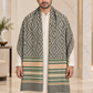 A man wearing a long gray and beige patterned shawl with green and cream stripes and white fringe, draped over a white kurta in an elegant indoor setting.