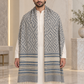 A man wearing a long, open-front shawl with a blue and gray geometric pattern and fringe, draped over a white kurta in an elegant indoor setting.