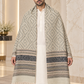 A man wearing a long beige and gray patterned shawl with fringe over a white kurta, standing in a marble-finished indoor setting.