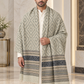 A man wearing a long, patterned shawl over a white kurta in an elegant indoor setting with marble walls and floors.