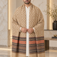 A man wearing a beige and brown patterned shawl with fringed ends over a white kurta, standing in a marble hallway.