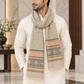 A man wearing a cream-colored kurta and a patterned beige scarf with geometric and striped designs in brown, orange, and gray, standing in a marble hallway.