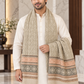 A man wearing a cream-colored kurta and a beige patterned scarf with peach and gray geometric borders, standing in a marble-floored indoor setting.