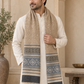 A man wearing a cream kurta and a beige woolen scarf with blue-gray geometric patterns, standing in a warm-toned architectural setting