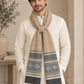 A man wearing a cream-colored kurta and a thick beige scarf with blue and gray geometric patterns and fringed ends, standing in a warm, neutral-toned indoor setting.