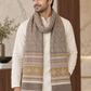 A man wearing a cream kurta and a thick, patterned beige and brown knit scarf with fringed ends, standing in a modern indoor setting.