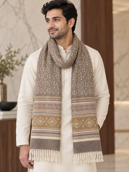 A man wearing a cream kurta and a thick, patterned beige and brown knit scarf with fringed ends, standing in a modern indoor setting.