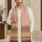 A man wearing a white kurta and trousers models a patterned scarf with a dusty pink upper section, a wide mustard-gold middle band, and a deep maroon lower section with fringe.