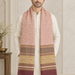 A man wearing a cream-colored kurta and a long, patterned pink and gold scarf with fringed ends, standing in a decorated indoor setting.